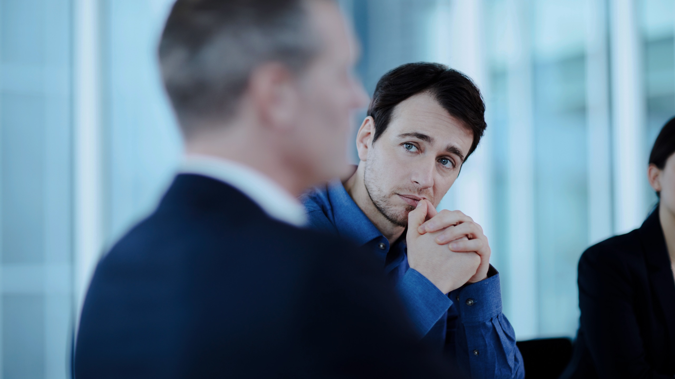 A senior executive pausing in thought during a high-pressure institutional meeting.