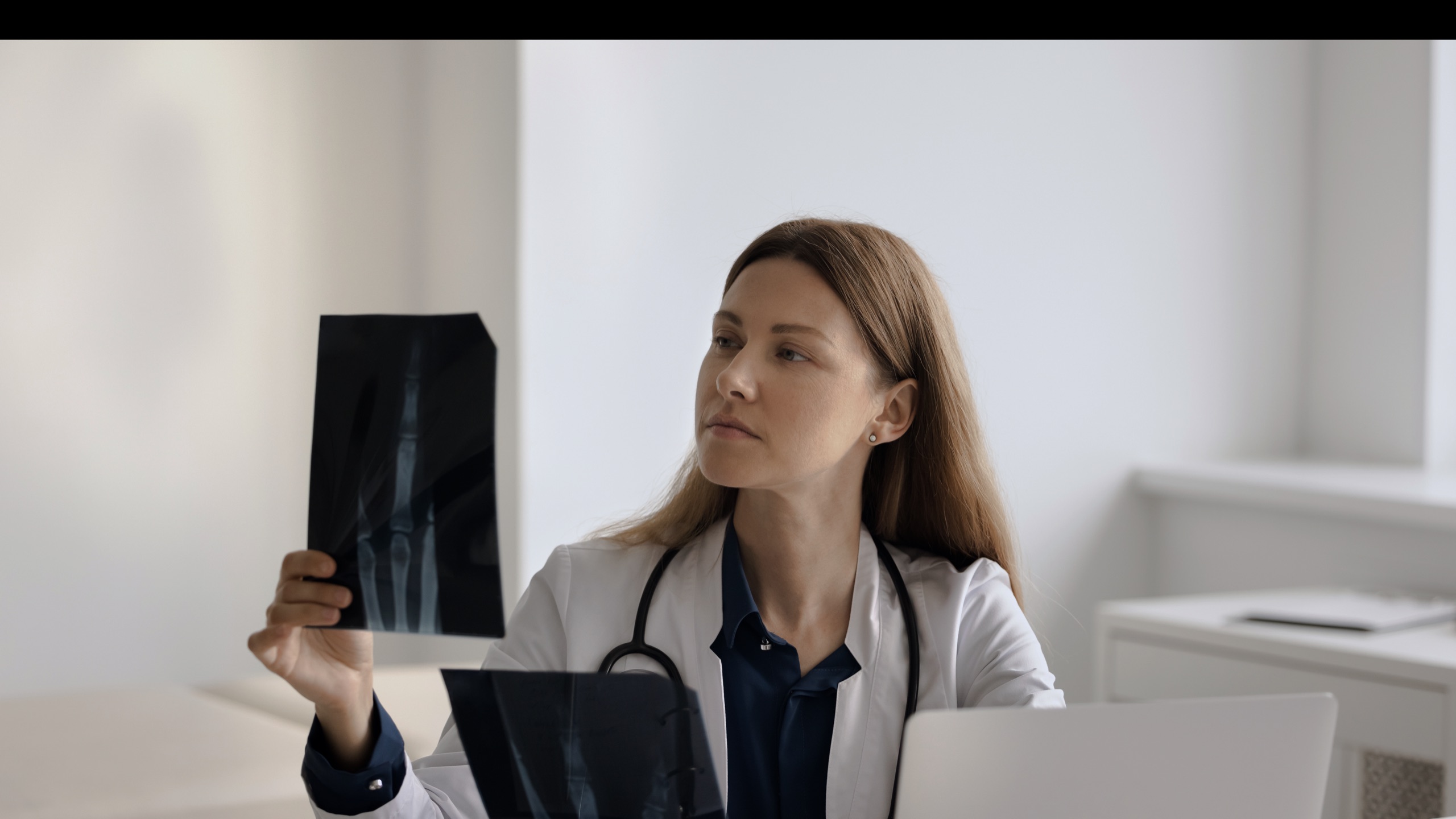 A physician studying diagnostic imaging at her desk, weighing the scan against her own clinical judgment.