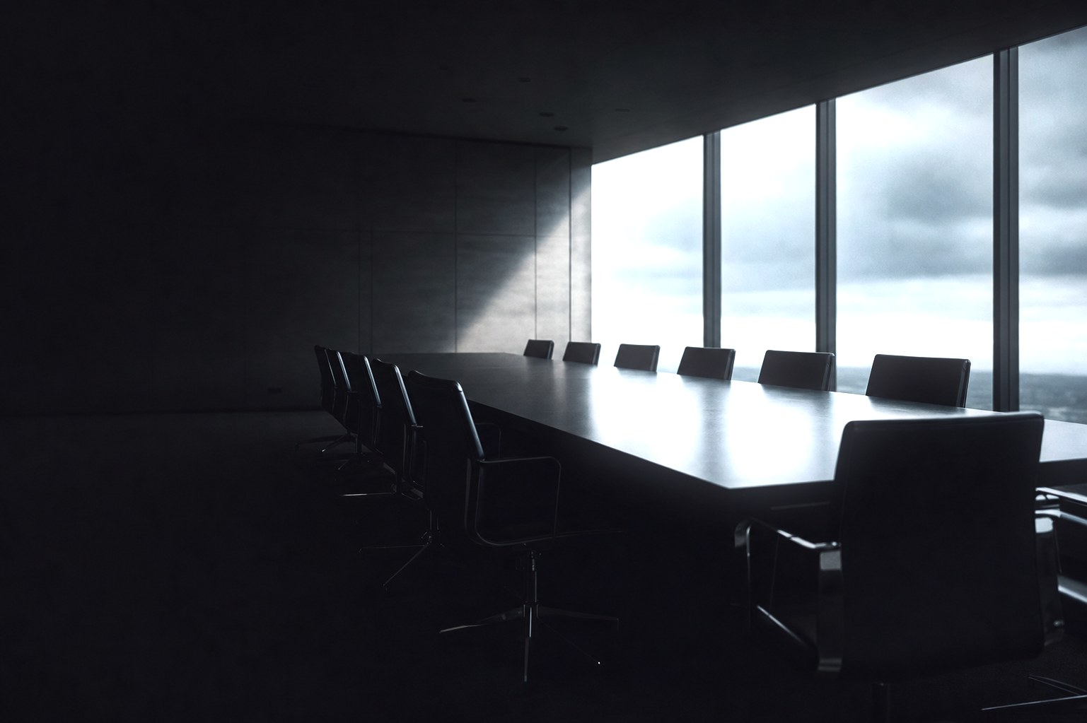 An empty boardroom in low light, a long dark table flanked by leather chairs, floor-to-ceiling windows opening onto an overcast sky.
