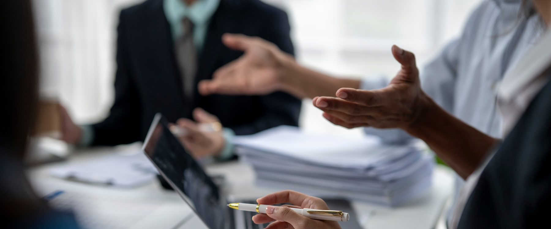 Several people around a table mid-discussion, hands and papers in view, working through a decision together.