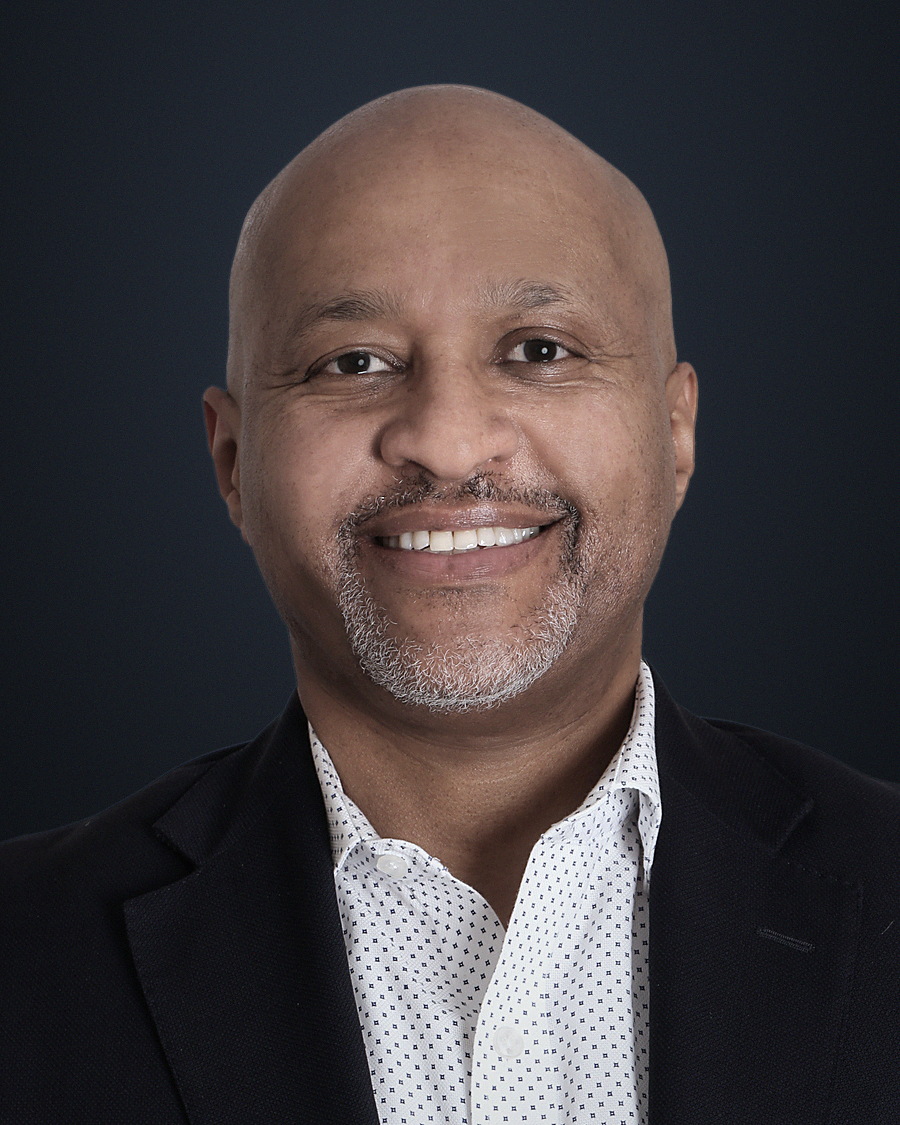 Ambaw Bellete, photographed from mid-chest against a dark background, in a dark suit jacket.
