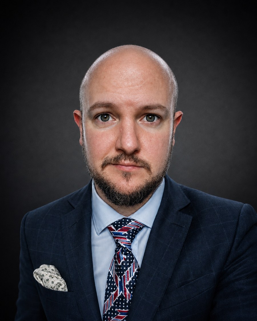 Vittorio Nigrelli, photographed head and shoulders in a dark checked suit against a dark background.